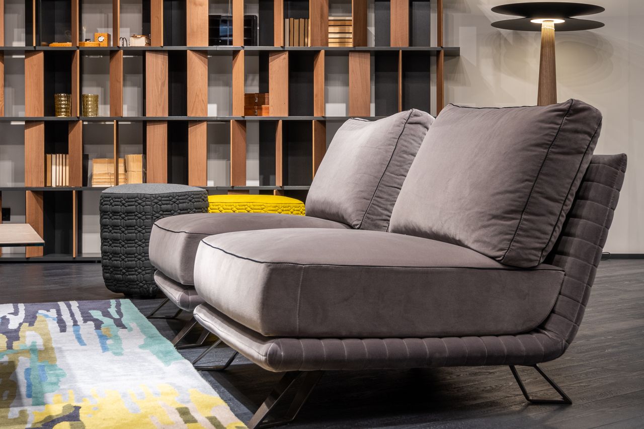 Interior design of modern living room furnished with comfortable settee with poufs against bookcase and shining lamp