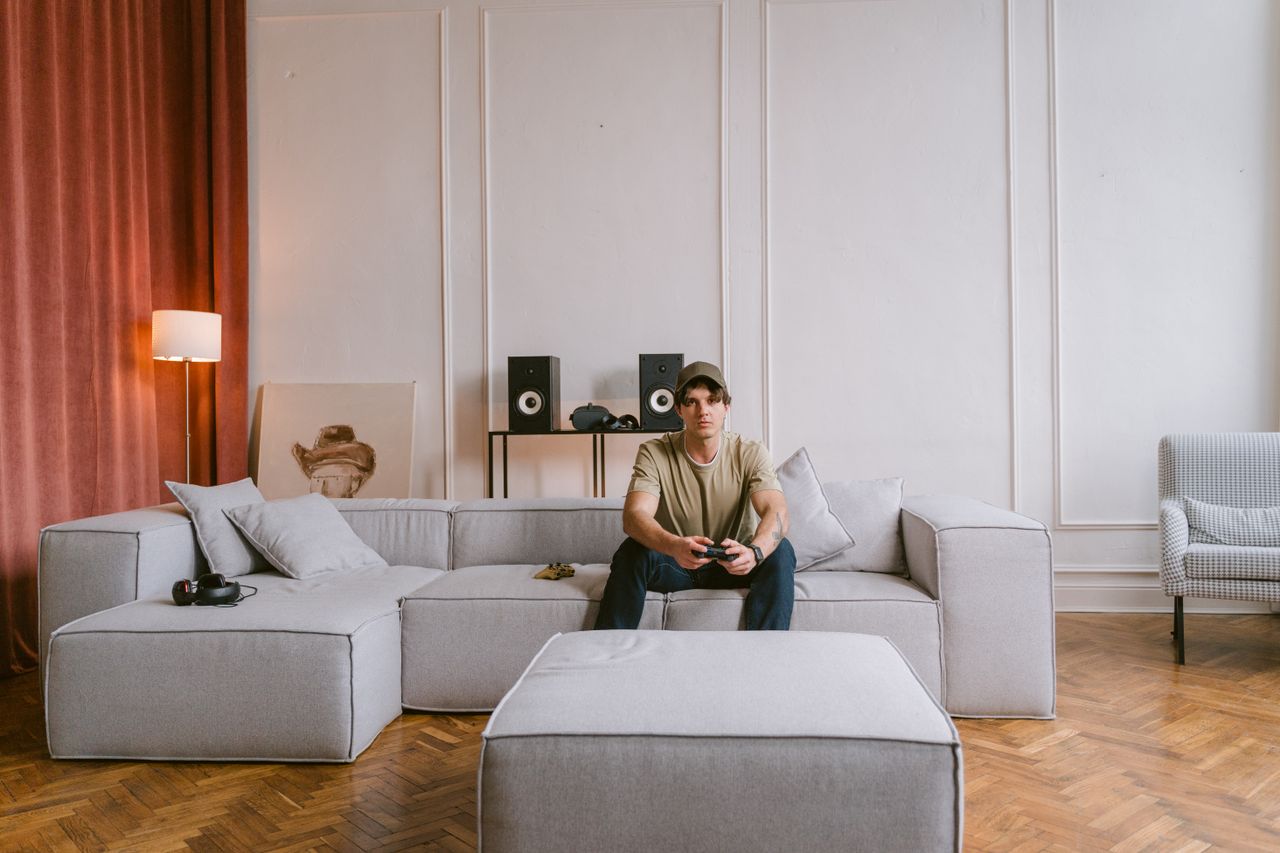 A young man sits on a modern sofa playing video games in a stylish living room interior.